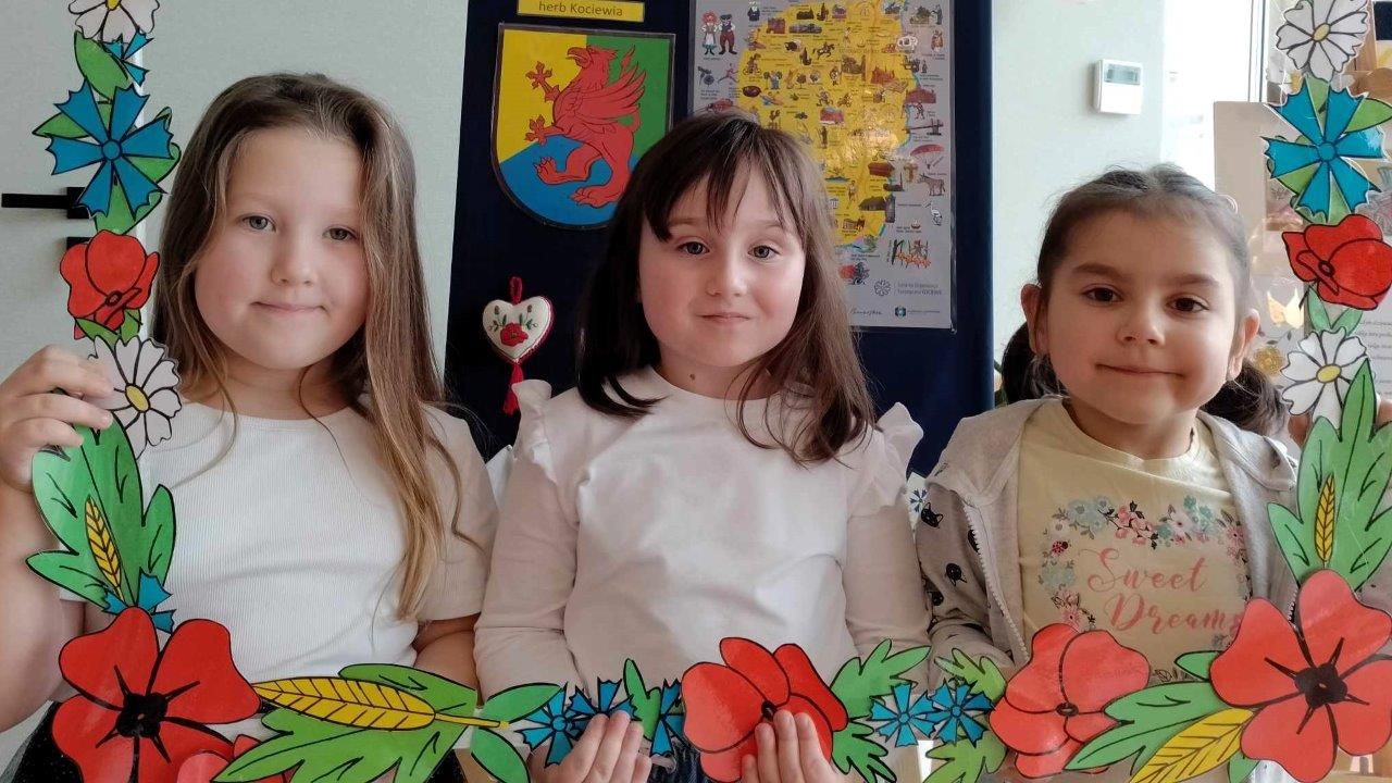 Trzy dziewczynki z przedszkola w Zblewie trzymają ramkę z kwiatkami